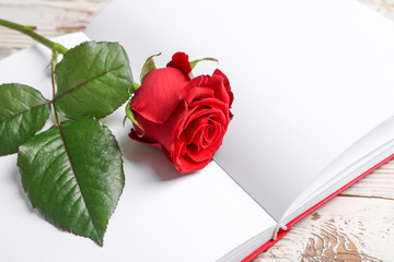 Beautiful rose and blank notebook on wooden background, closeup. Valentine's Day celebration