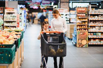 beautiful mother holding grocery basket with her child walking in supermarket. Shopping for healthy.