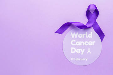 Paper with text WORLD CANCER DAY and purple ribbon on color background