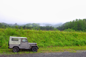 Military vehicles parked on a gravel road The background is trees and grass and mountains with fog in the morning.