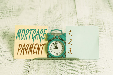 Conceptual hand writing showing Mortgage Payment. Concept meaning periodic amount paid to a holder for repayment of a loan Mini blue clock standing above buffer wire between two paper