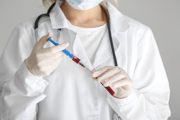 Laboratory assistant holding syringe and test tube with blood sample in clinic, closeup