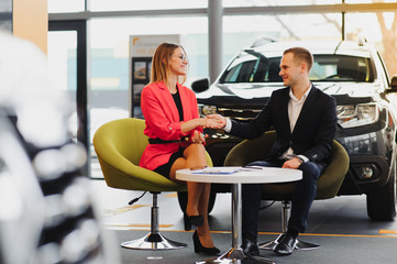 Beautiful young woman buys a car in the dealership saloon.