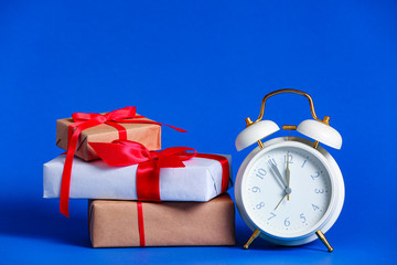 Alarm clock with Christmas gifts on color background