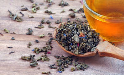 blended tea. green tea with dry flower petals. dry leaves of green tea in a wooden spoon and glass...