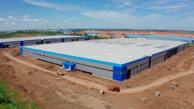 trucks drive along warehouse at construction site aerial