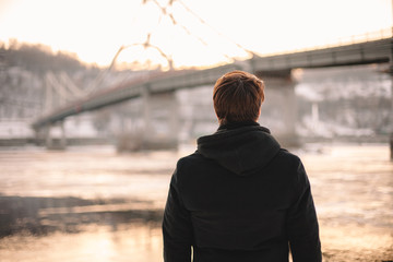 Back view of thoughtful young man looking at river while standing outdoors in winter