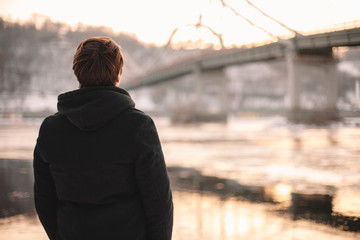 Back view of thoughtful young man standing by river in winter - Powered by Adobe