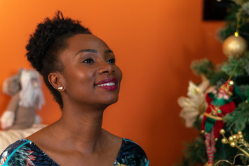 Afro-descendant Colombian woman sitting on the sofa next to the Christmas tree smiling happy