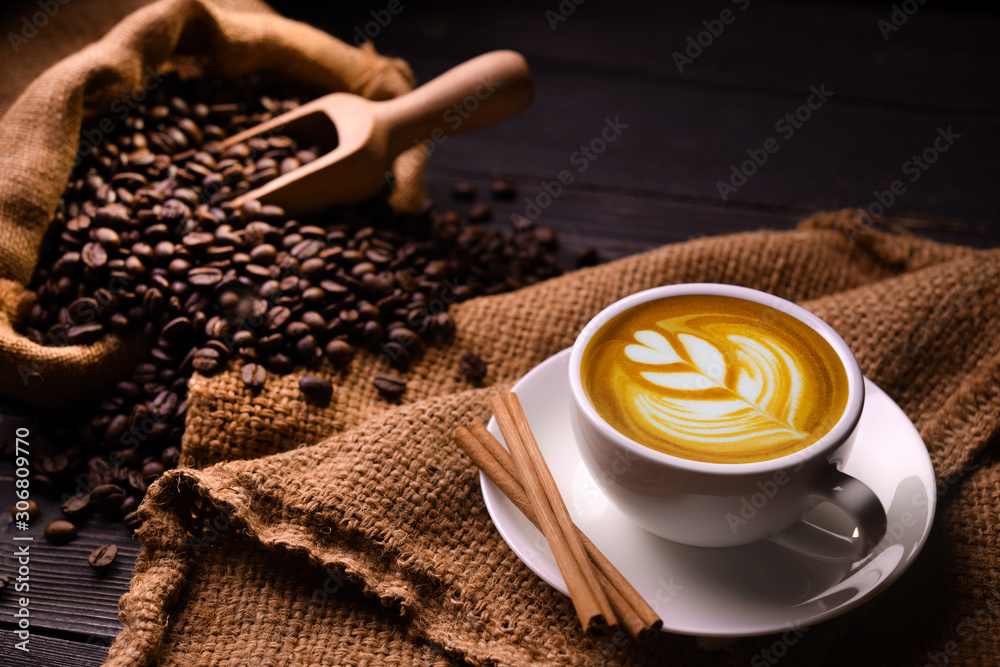 Wall mural Cup of coffee latte and coffee beans in burlap sack on old wooden background