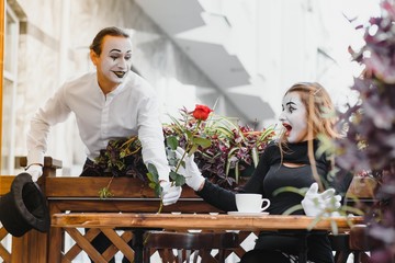 mime guy and girl in cafe drinking coffee. Mime in front of Paris cafe acting like drinking tea or coffee.