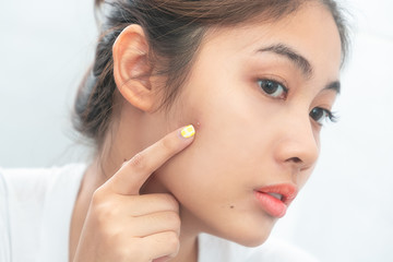 Beautiful girl is squeezing pimples on her face while looking into the mirror.