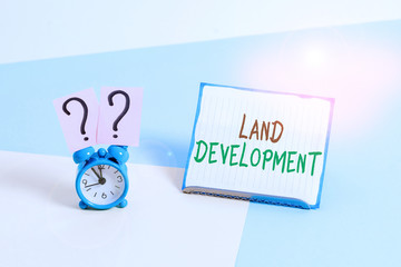 Conceptual hand writing showing Land Development. Concept meaning process of acquiring land for constructing infrastructures Alarm clock beside a Paper sheet placed on pastel backdrop