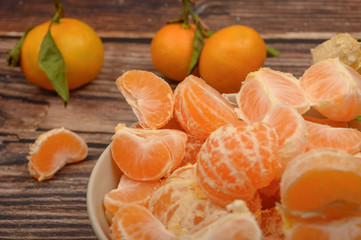 Peeled tangerines in a ceramic dish, tangerines on a twig with green leaves on a wooden background. Autumn harvest. Close up.