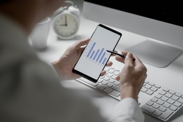 Close up shot of businessman working in office holding smart phone and checking diagrams