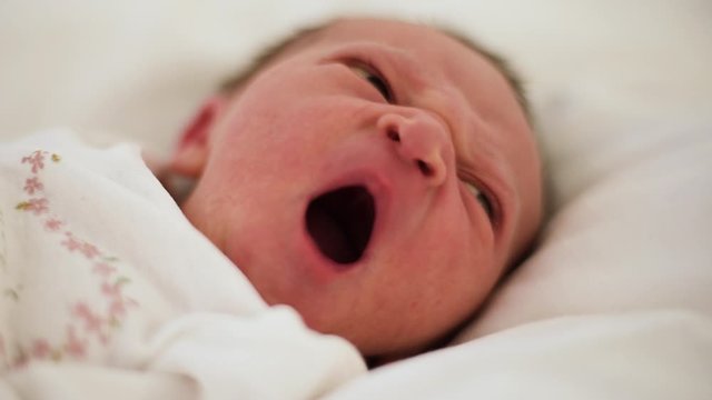 Yawning tiny newborn baby with long dark hairs. One day old baby.