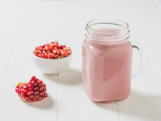 Freshly made pomegranate smoothie and pomegranate seeds on a white table.
