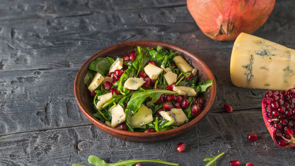 A piece of blue-mold cheese and arugula and pomegranate salad on a rustic table.