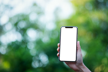 Mockup image of a hand holding black mobile phone with blank desktop screen with green nature background