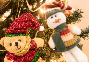 Bear and snowman christmas toys with red and green clothes on Christmas tree with yellow lights