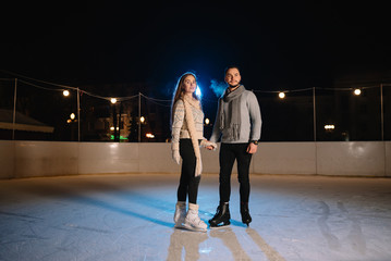 Winter skates, loving couple holding hands and rolling on rink. Illumination in background, night. Concept training.