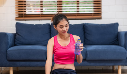Fototapeta na wymiar Young asian woman take a rest after training and drinking water after workout in living room