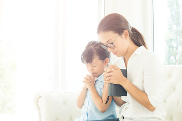 Religious Christian girl praying with her mother indoors