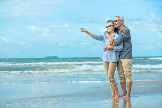 Side view of romantic senior couple while standing hugging each other while at beach and pointing hands forward. image not focus. Retirement age concept and love.