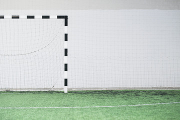 Part of empty football field, gates and net against white wall on stadium