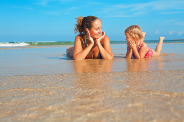 Happy people have fun in sea surf on white sand beach. Young mother with child lying in water pool....