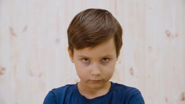 Portrait serious boy looking to camera on light background in studio. Close up face young boy posing to camera Facial children emotions