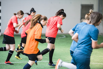 Group of active female footballers in sports uniform running down the field
