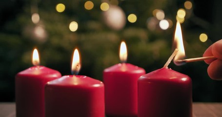 light the fourth red candle of an advent wreath in front of a christmas tree