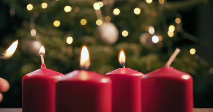 light the third red candle of an advent wreath in front of a christmas tree
