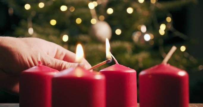 light the second red candle of an advent wreath in front of a christmas tree