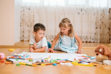 Fototapeta premium Kids drawing on floor on paper. Preschool boy and girl play on floor with educational toys - blocks, train, railroad, plane. Toys for preschool and kindergarten. Children at home or daycare.