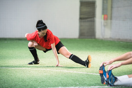Active girl in sports uniform doing exercise for stretching legs before game