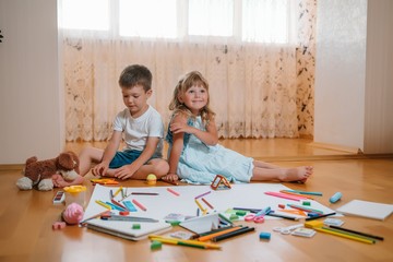 Kids drawing on floor on paper. Preschool boy and girl play on floor with educational toys - blocks, train, railroad, plane. Toys for preschool and kindergarten. Children at home or daycare.