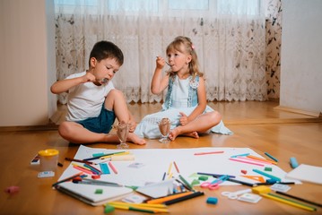 Kids drawing on floor on paper. Preschool boy and girl play on floor with educational toys - blocks, train, railroad, plane. Toys for preschool and kindergarten. Children at home or daycare.