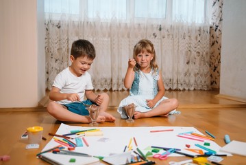 Obraz premium Kids drawing on floor on paper. Preschool boy and girl play on floor with educational toys - blocks, train, railroad, plane. Toys for preschool and kindergarten. Children at home or daycare.