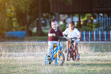 Cute asian child boy and his old sister having fun to ride a bicycle together in the park