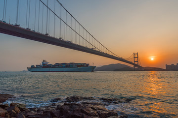 Cargo ship and suspension bridge in Hong Kong city under sunset