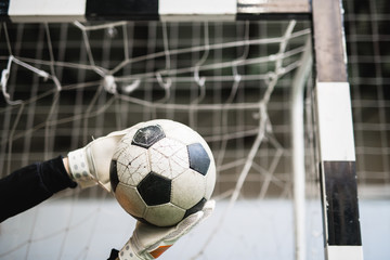 Gloved hands of successful goalkeeper caught soccer ball against net in gate