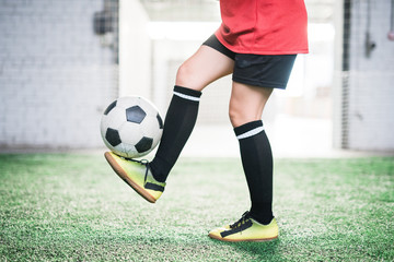 Low section of young female football player with soccer ball over foot