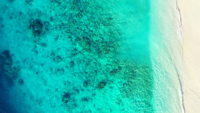 Beautiful sea texture with rocks and corals over seabed seen through turquoise clear water of lagoon washing white sand of exotic beach, copy space
