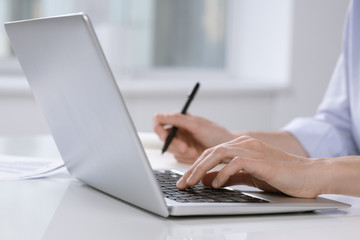 Hand of female employee pushing buttons of laptop keypad while sitting by desk