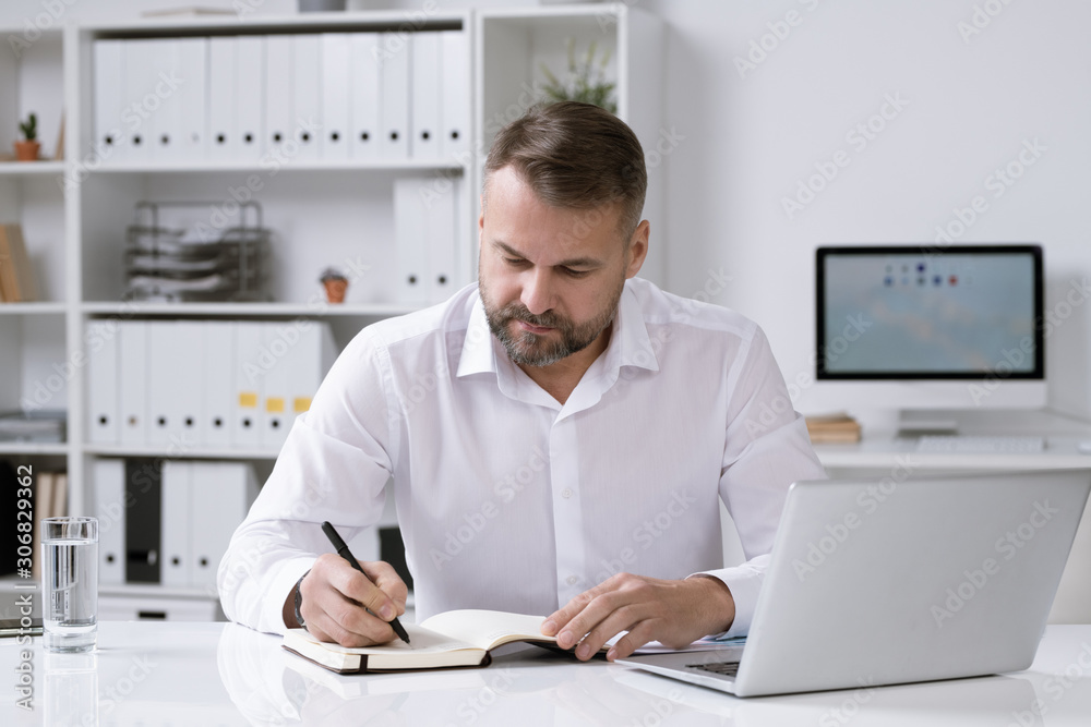 Poster serious bearded businessman thinking of ideas and making notes in notebook