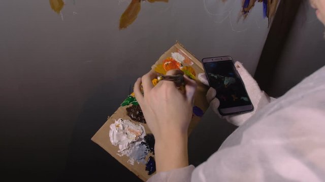 Artist designer draws an eagle on the wall. Craftsman decorator paints a picture with acrylic oil color looking at the sketch in the phone. Indoor. Dark magic cinematic look.
