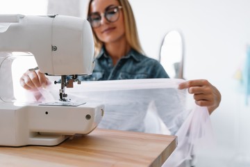 Smiling fashion designer looking at camera at workplace, dressmaker, needlewoman or tailor shop owner sitting at desk with color swatches pantone and embroidery design sketches on the wall, portrait