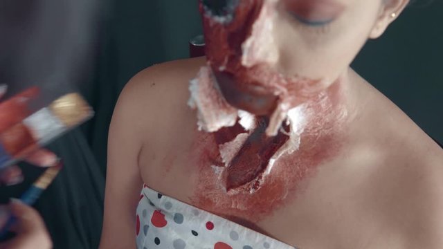 Close up of professional artist making a zombie scary mask on woman's face for Halloween 